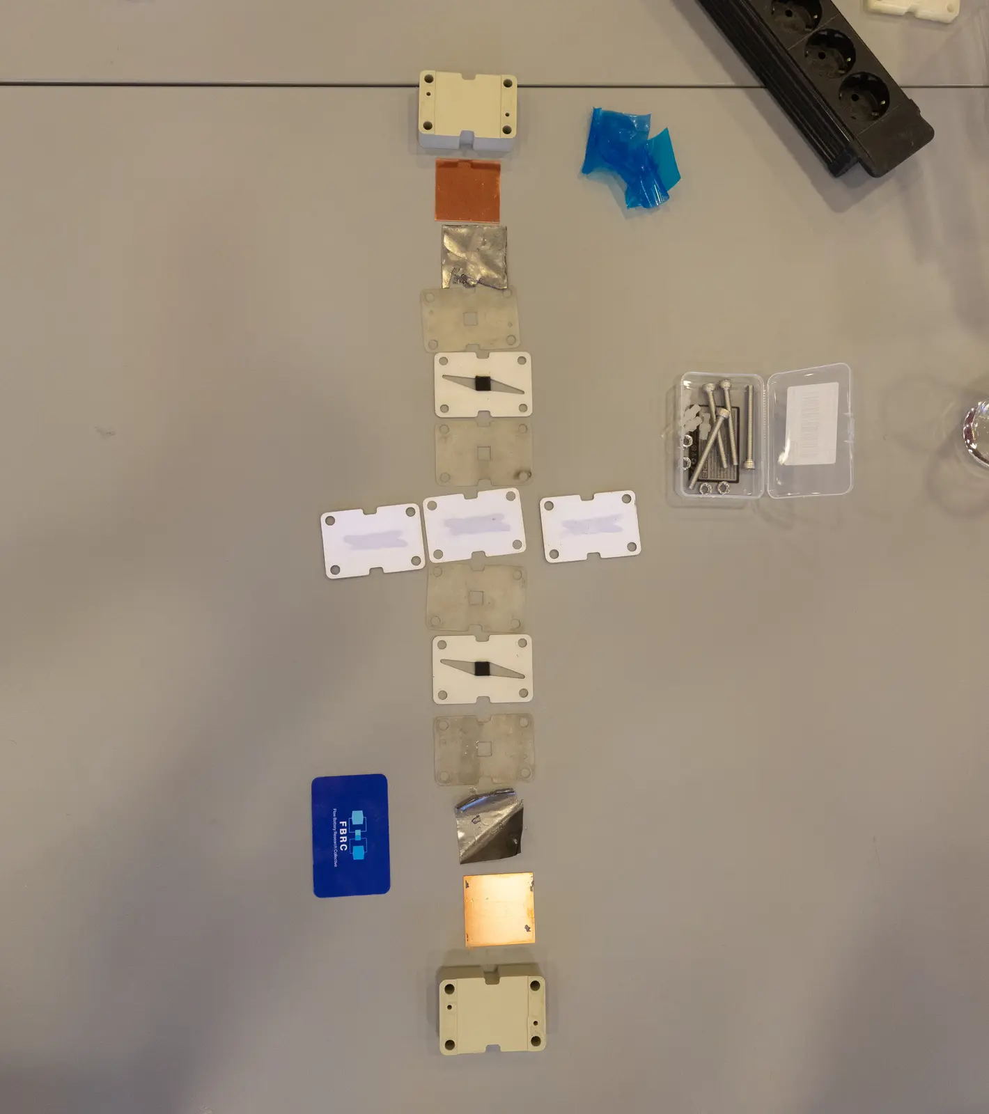 The components of the flow battery test cell individually laid out on a table, arranged in order of assembly